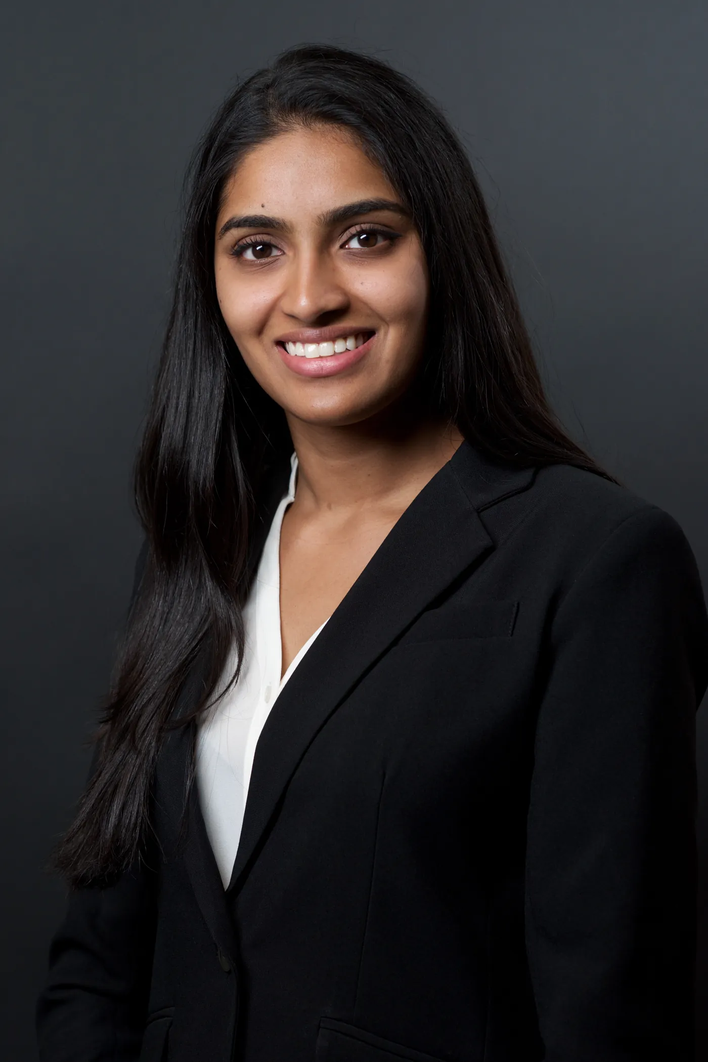 Smiling corporate headshot of a woman in a black suit, dark studio backdrop