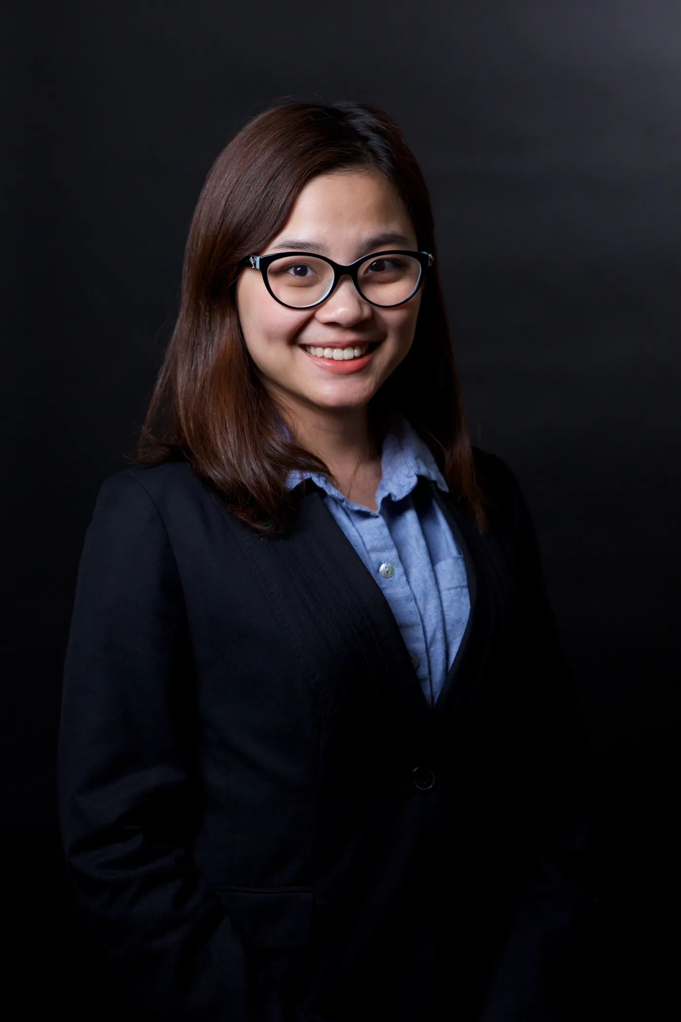 Corporate headshot of a woman in glasses on a near-black backdrop