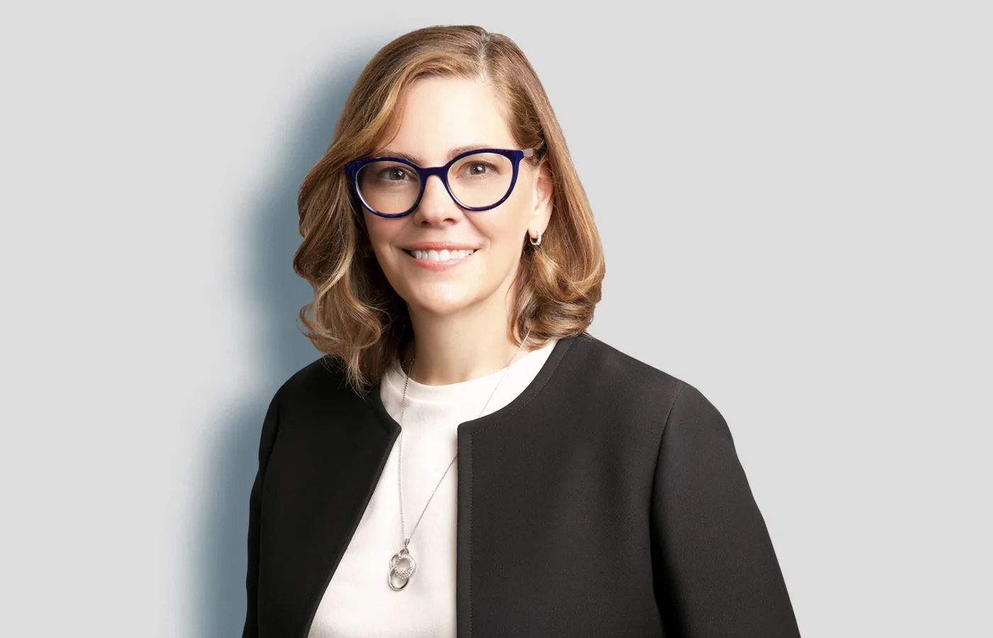 Team headshot of a woman in glasses and a black jacket on a light gray backdrop