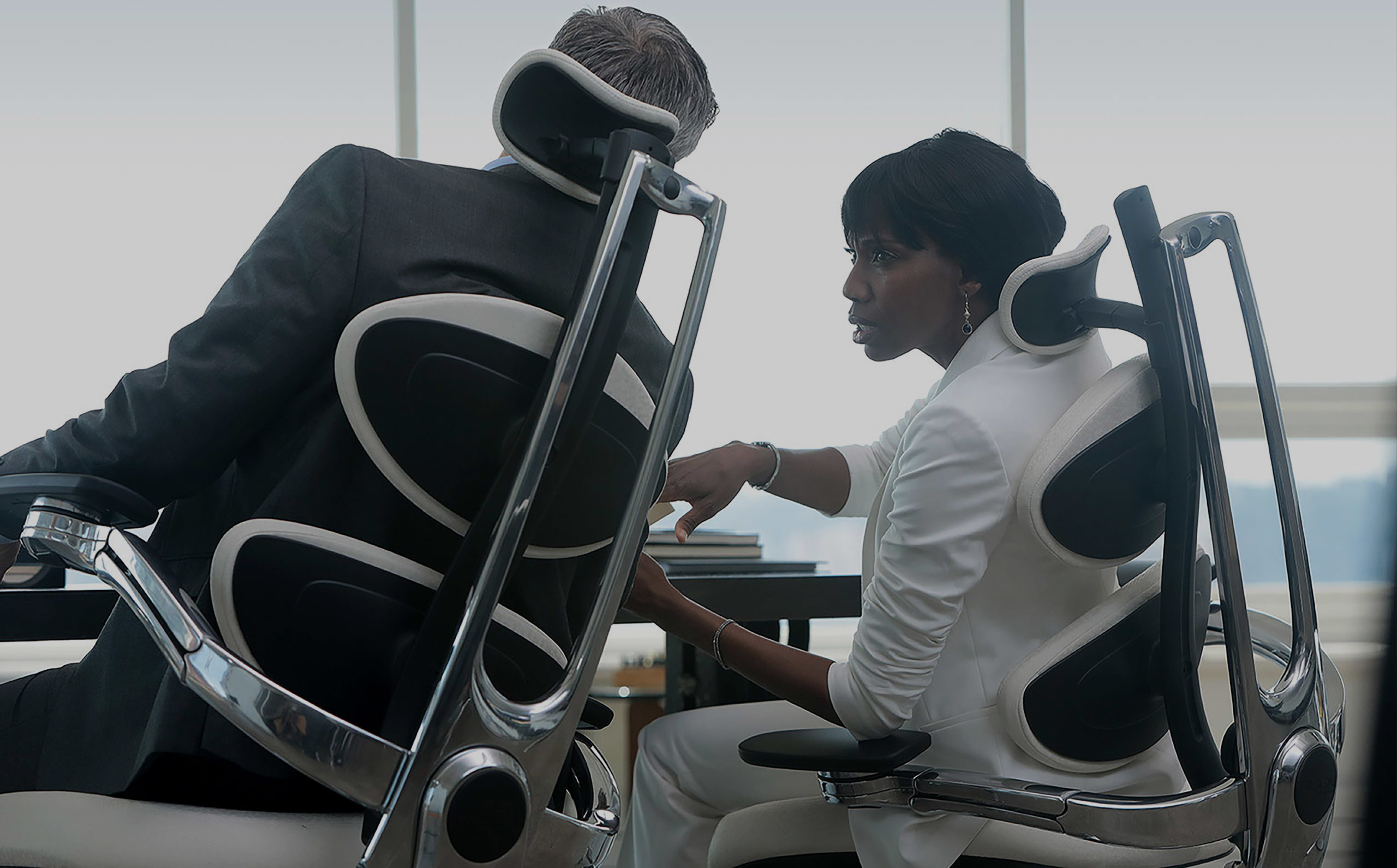 Commercial photography — two people working on MUUV ergonomic chairs in a dark office