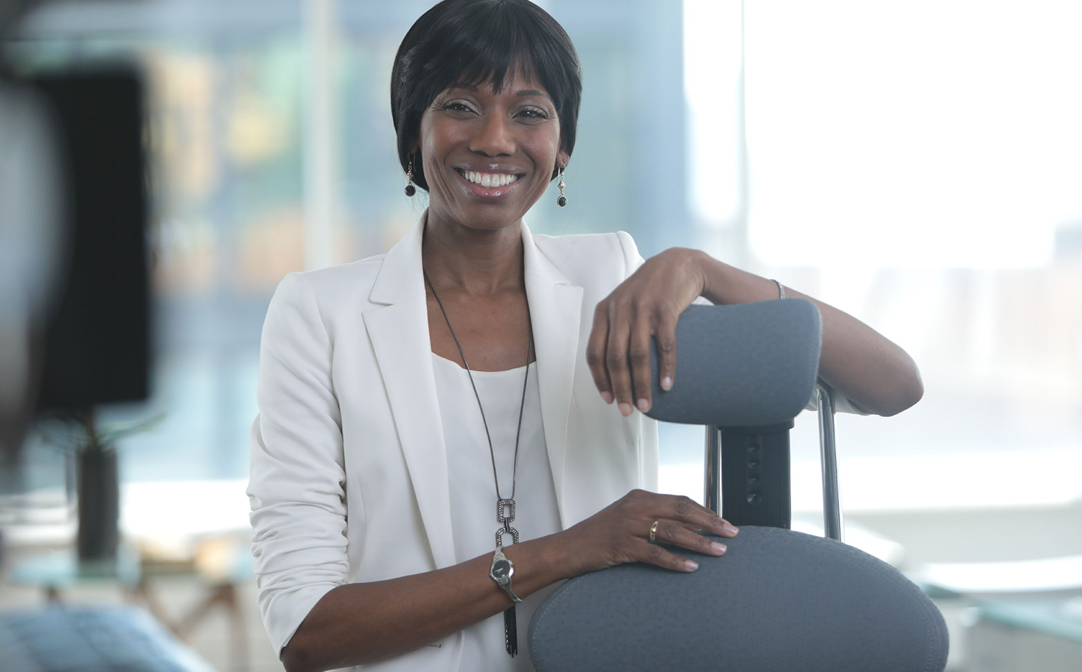 Environmental portrait — smiling woman in white blazer seated in a modern office